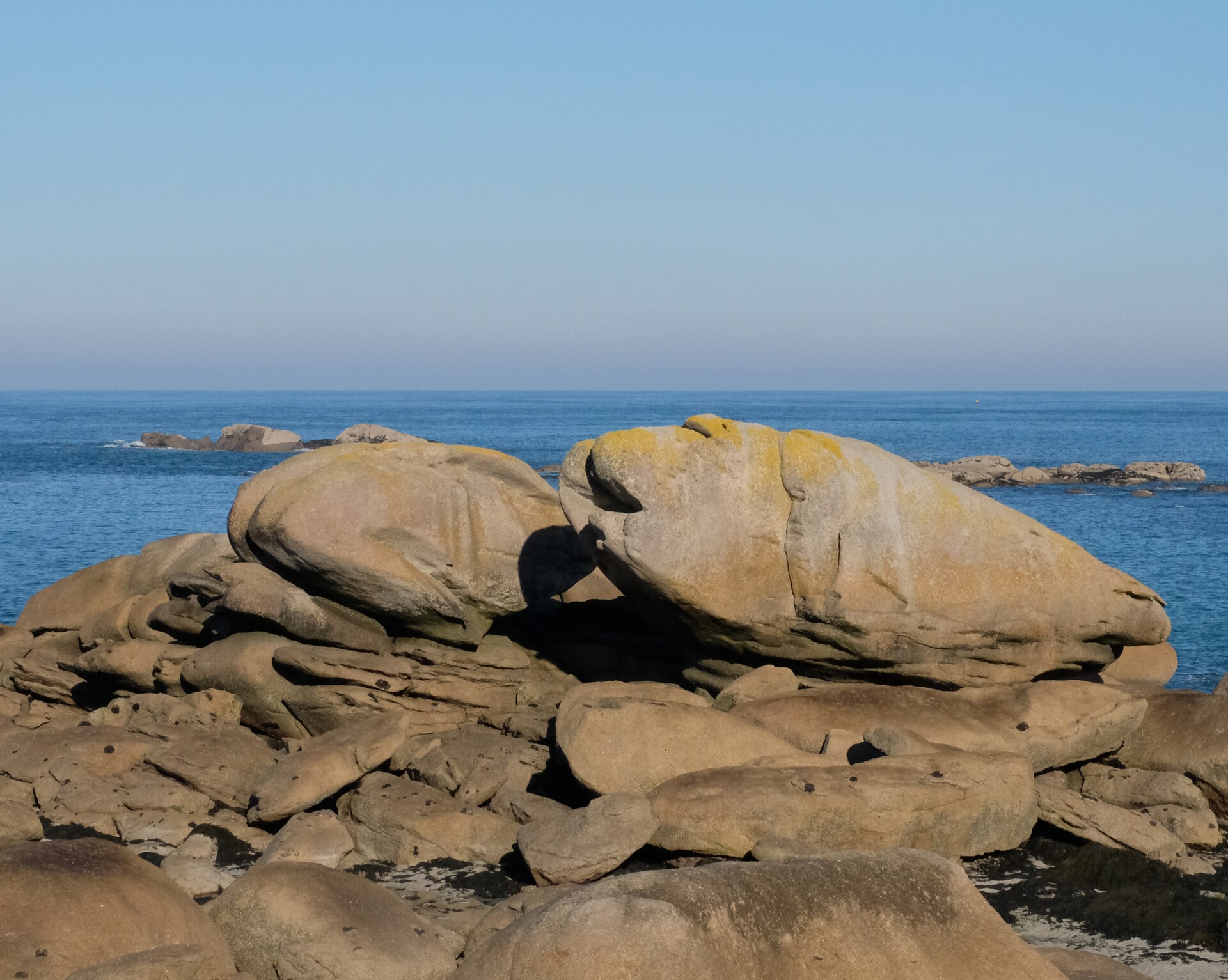 De gros rochers de granit rose au bord de l'eau, sous un ciel bleu