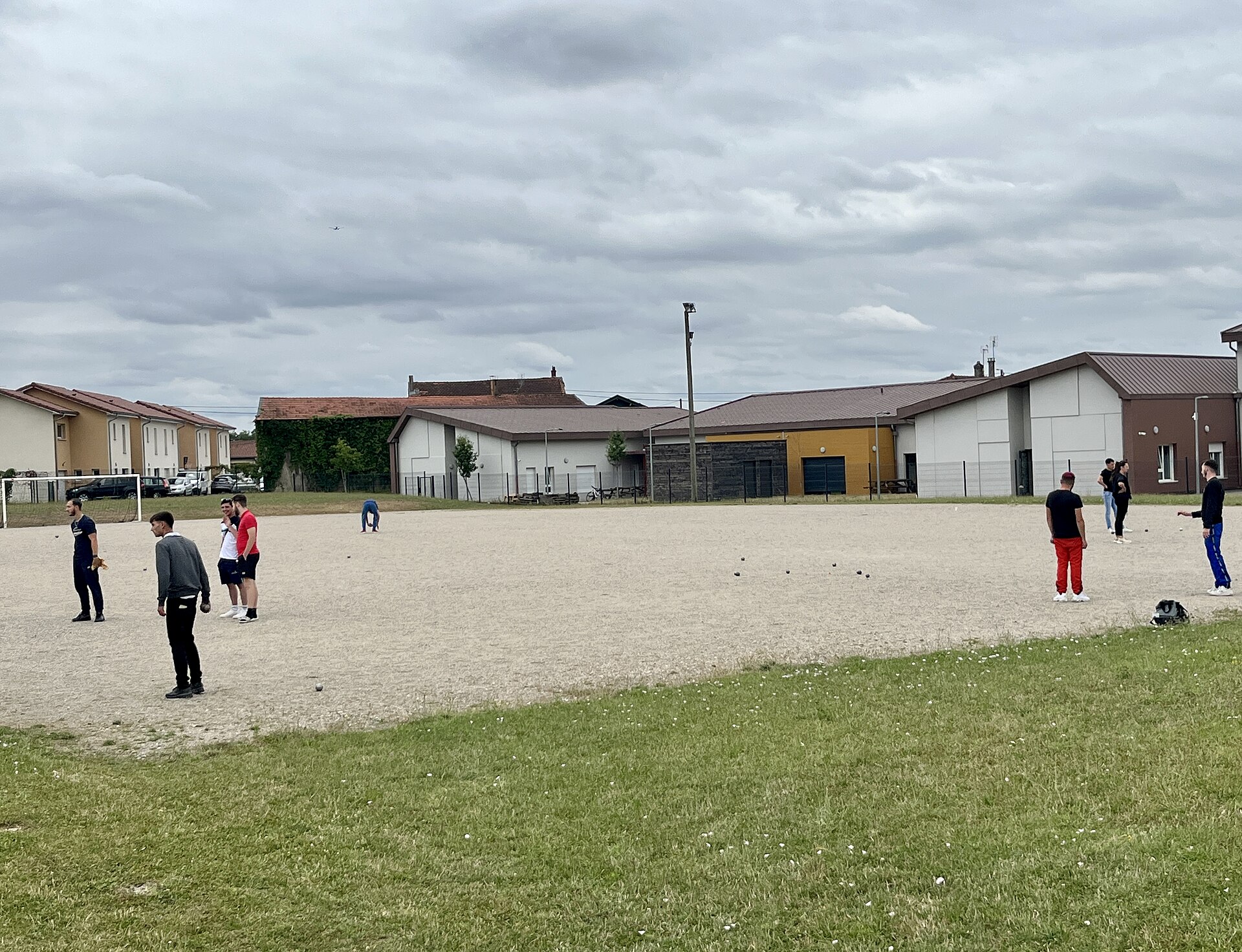 Le terrain de boules de l'espace sportif, quelques joueurs et les bâtiments du complexe